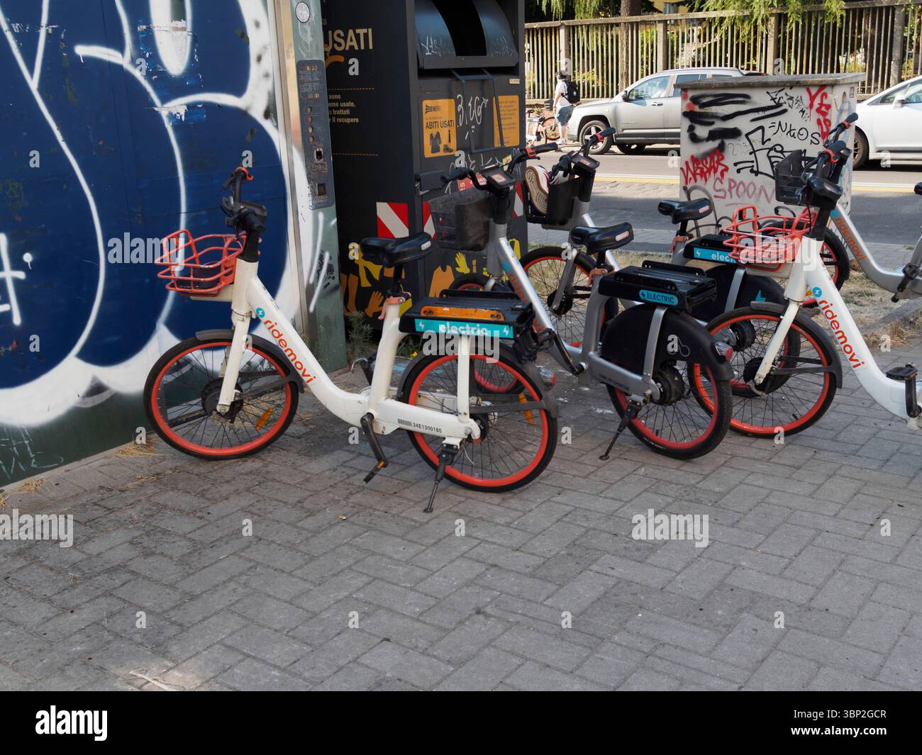 Bologna, Italien 3. Juli 2025 Weiße und graue Ridemovi Elektrofahrräder parken auf einem Mailänder Bürgersteig, umgeben von Graffiti und Mülltonnen, was hervorhebt Stockfoto