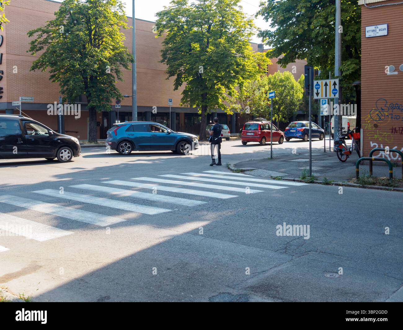 Bologna, Italien 3. Juli 2025 Verkehrsleiter, der eine Kreuzung in der Nähe von Crosswalk verwaltet und Fahrzeuge bei hellem Tageslicht in der Innenstadt Mailands führt Stockfoto