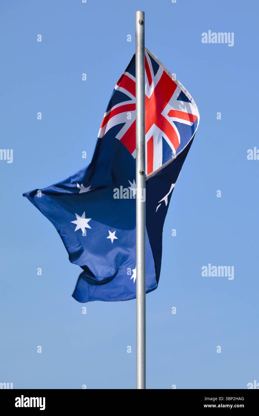 Die Nationalflagge Australiens fliegt stolz an einem wunderschönen Sommertag mit blauem Himmel auf einem Fahnenmast. Stockfoto