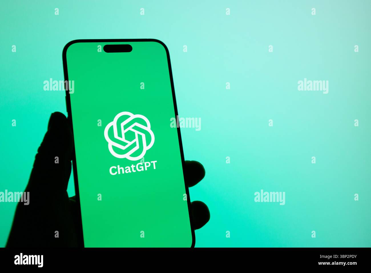 Ein Telefon wird mit grünem Hintergrund aufgehalten. Das Telefon hat ein ChatGPT-Logo Stockfoto