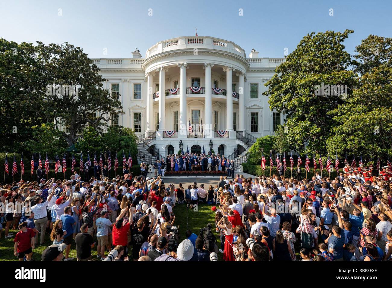 Eine große Menschenmenge versammelt sich vor dem Weißen Haus, das mit patriotischen roten, weißen und blauen Fahnen und einer Ausstellung amerikanischer Fahnen geschmückt ist. Zuschauer machen Fotos und beobachten eine Live-Zeremonie, die auf einer zentralen Bühne am Fuß des berühmten nördlichen Portico stattfindet. Die Szene fängt den Geist einer nationalen Feier ein, mit festlicher Einrichtung und einer lebhaften Atmosphäre, die Veranstaltungen zum Unabhängigkeitstag hervorhebt. Washington, D.C. | 4. Juli 2025 | Bild mit freundlicher Genehmigung des Weißen Hauses. Stockfoto