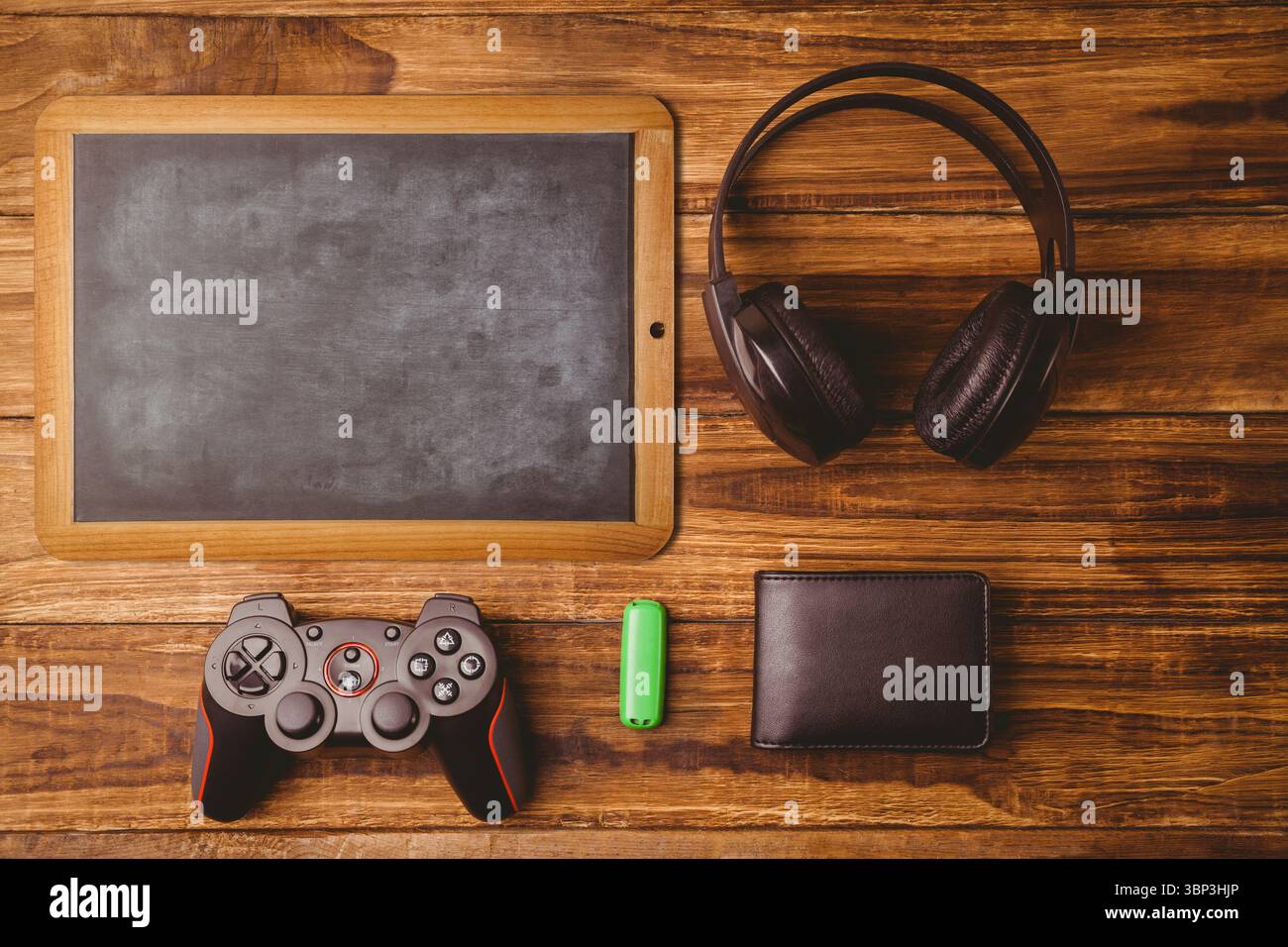 Flache Top-Down-Szene mit hölzerner Tafel, Kopfhörern, Controller, grünem USB-Laufwerk und Brieftasche Stockfoto