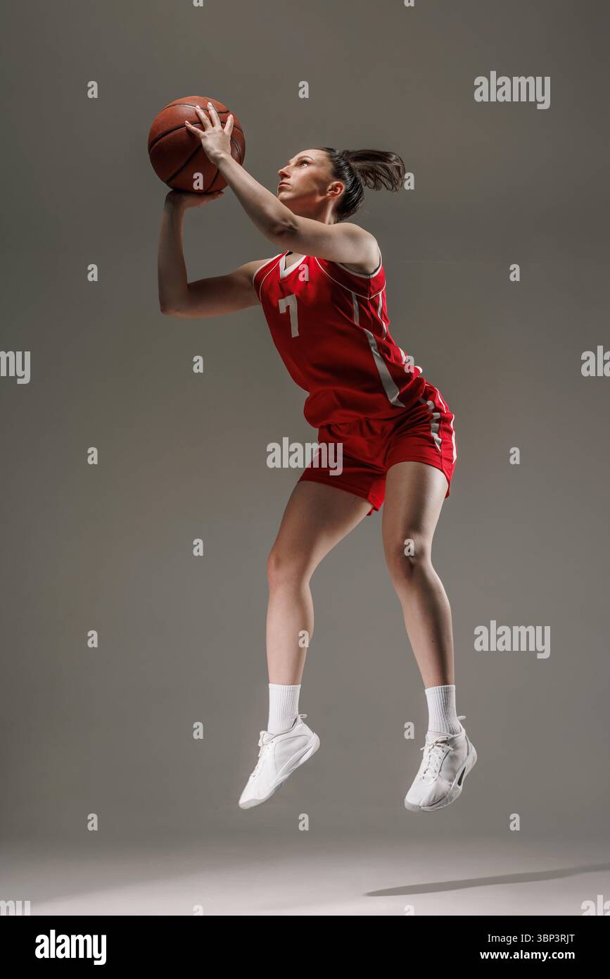 Fokussierte Basketballspielerin in roter Uniform, die für einen Schuss springt und dynamische Bewegung und sportliche Entschlossenheit zeigt. Stockfoto