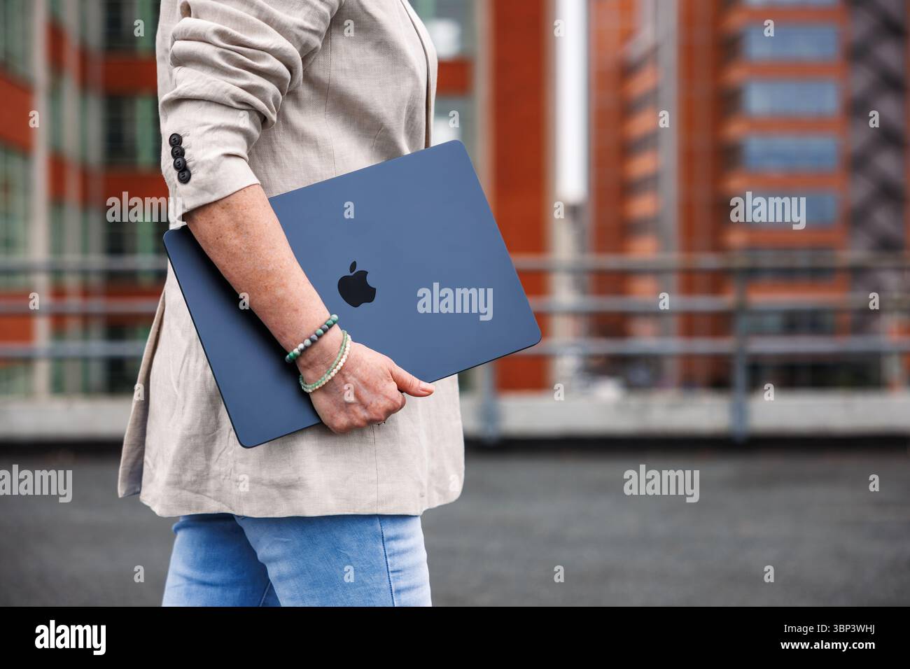 Zlin, Tschechische Republik - 13. April 2025: Geschäftsfrau mit Apple Laptop MacBook Air, die vor dem Bürogebäude läuft Stockfoto