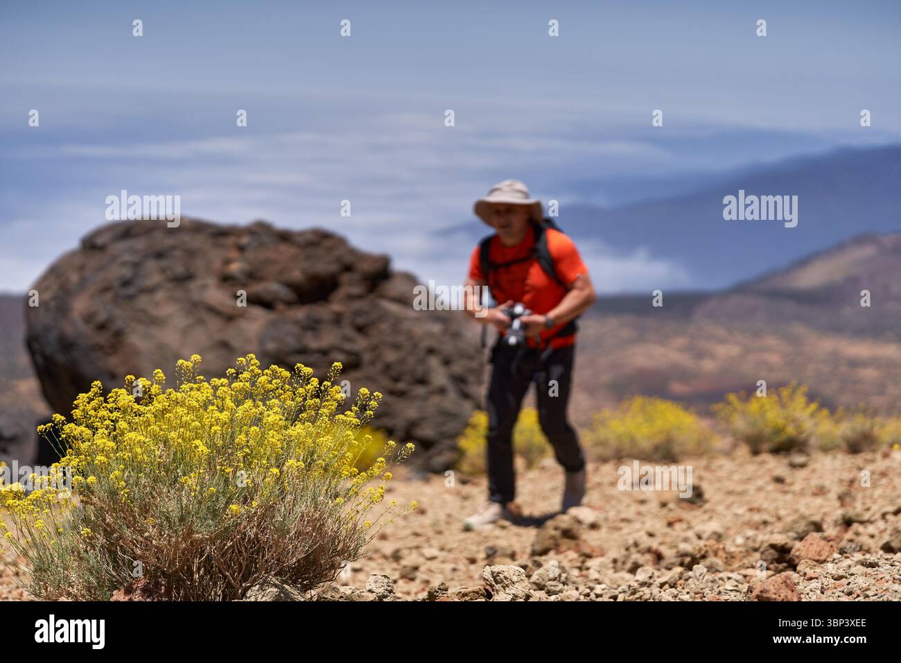 Mann wandert über felsiges vulkanisches Gelände mit Kamera in der Hand und Berglandschaft im Hintergrund Stockfoto
