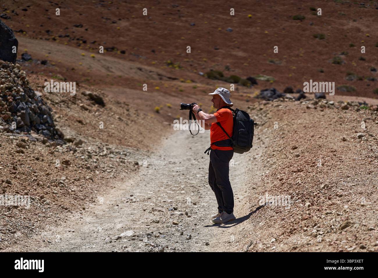 Mann wandert über felsiges vulkanisches Gelände mit Kamera in der Hand und Berglandschaft im Hintergrund Stockfoto