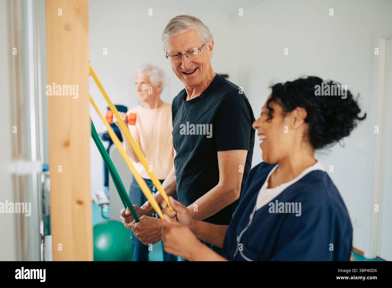 Glücklicher Seniorenmann, der mit Hilfe einer Therapeutin im Reha-Zentrum Widerstandskorrektur zieht Stockfoto