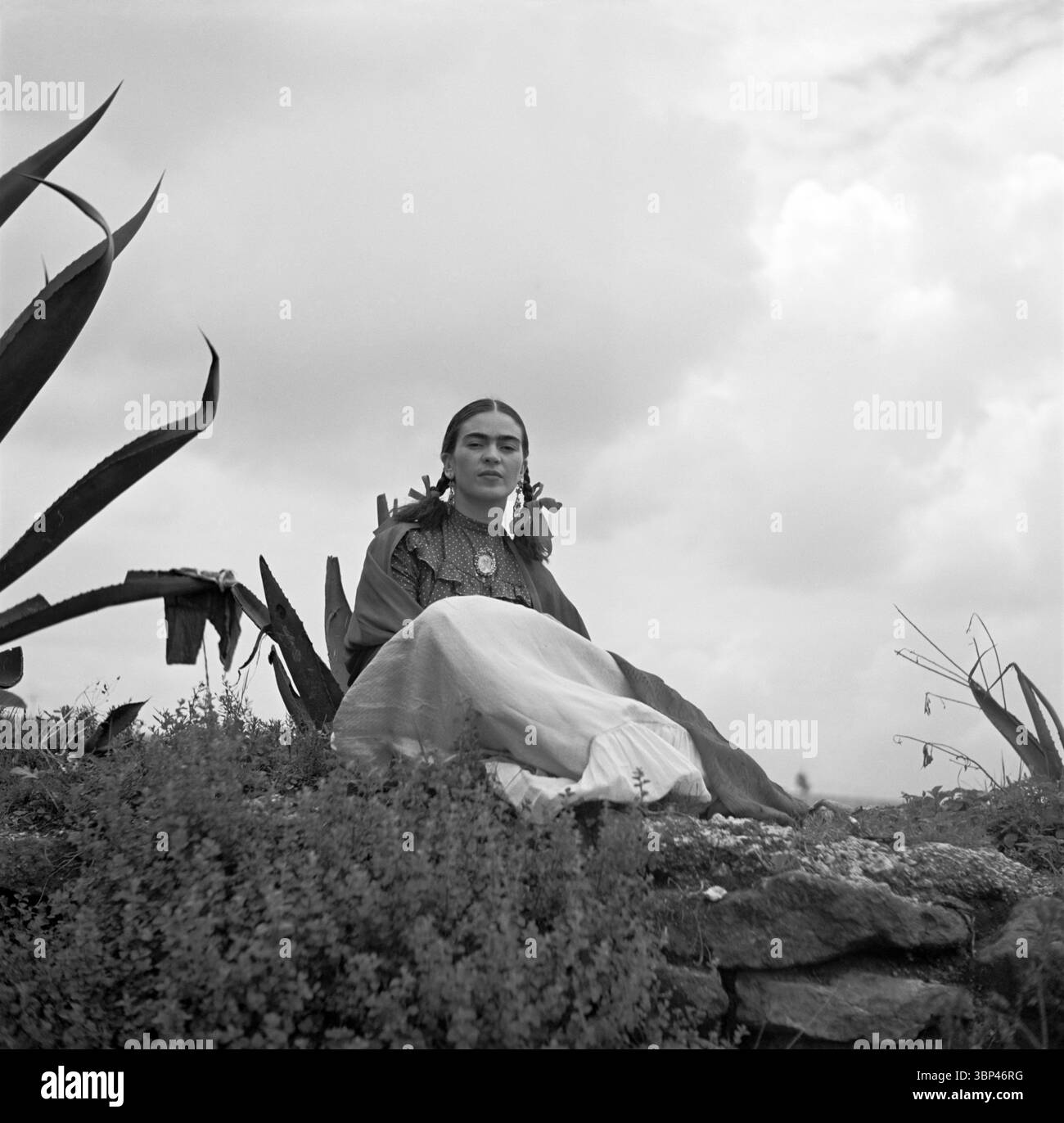Eine Fotografie von Frida Kahlo, aufgenommen von Toni Frissell (1907–1988), die 1937 im Freien zwischen Agavenpflanzen saß und traditionelle mexikanische Kleidung trug. Toni Frissell war eine US-amerikanische Fotografin, die für ihre Modefotografie, ihren Fotojournalismus und ihre Porträts bekannt war. Ihre Fotografien von Frida Kahlo sind bedeutend, da sie die Künstlerin in einer entspannteren und natürlicheren Umgebung einfangen und eine andere Perspektive bieten als die oft hochinszenierten Selbstporträts, die Kahlo schuf. Dieses Bild wurde für das Vogue Magazin „Senoras of Mexico“ während Kahlos Besuch in New York aufgenommen. 1937. Stockfoto
