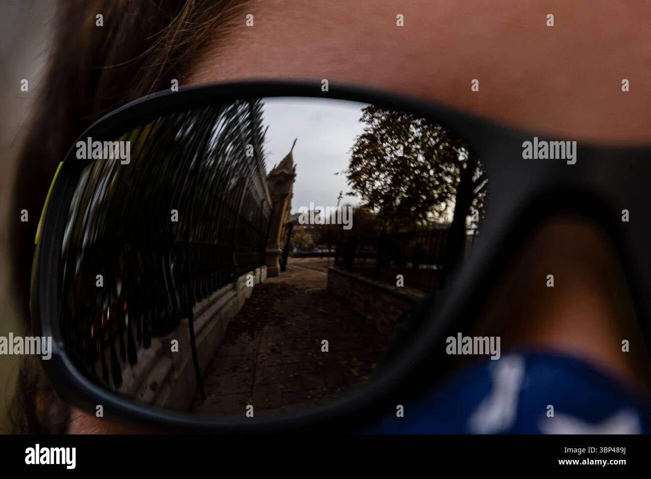 Die Sonnenbrille spiegelt ein markantes Gebäude wider, während eine Person an einem bewölkten Tag in einem Stadtpark steht. Stockfoto