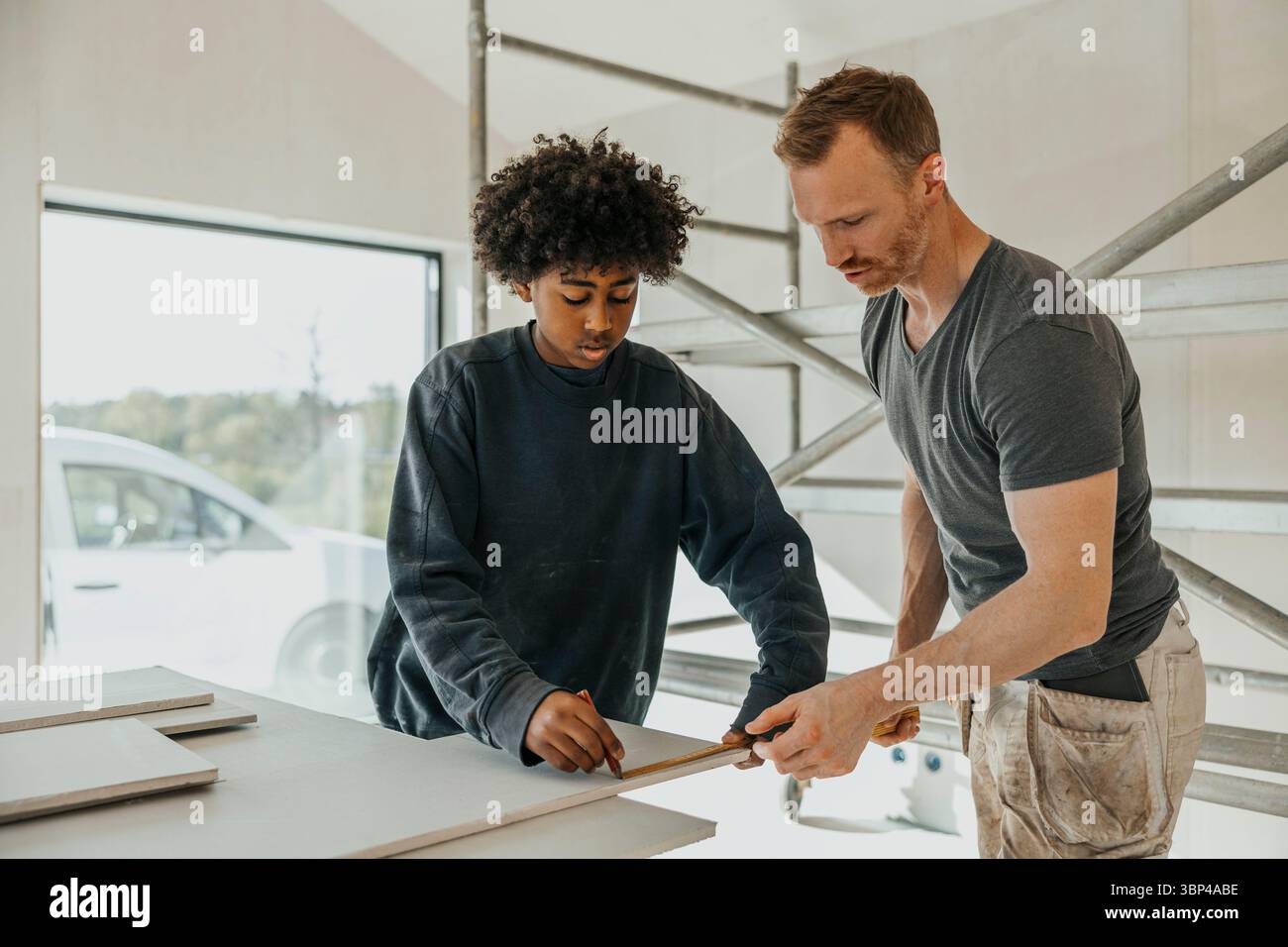 Fokussierte Bogenmarkierung von Holzdielen mit väterlicher Hilfe bei der Haussanierung Stockfoto