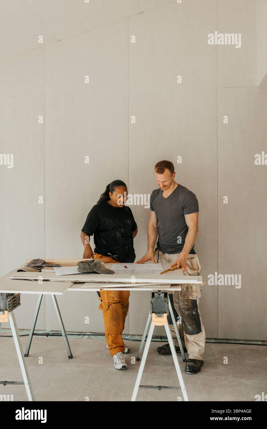 Multirassisches Paar diskutiert Wohnraumrenovierungsplan auf der Baustelle Stockfoto