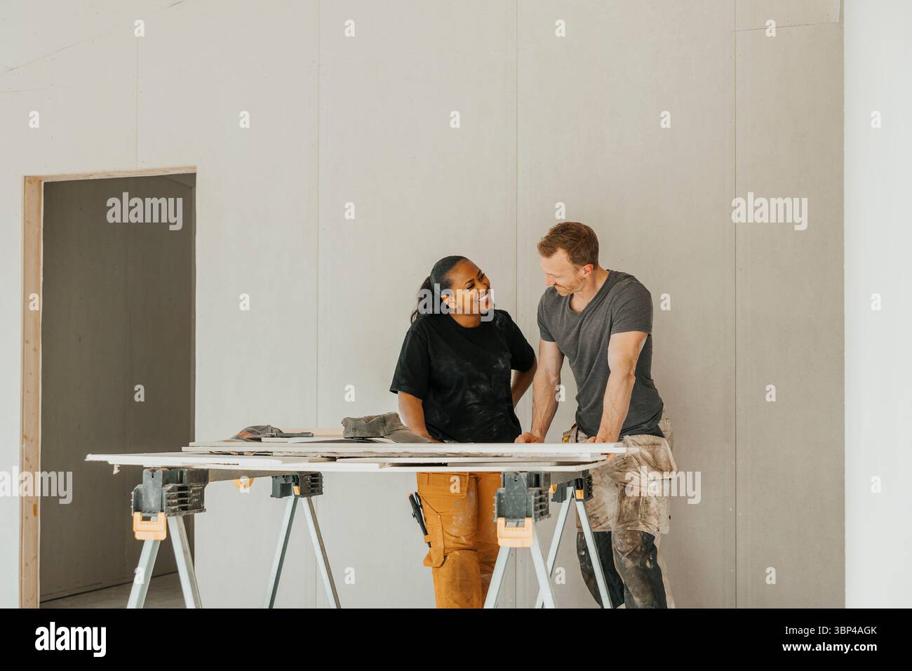 Lächelndes multirassisches Paar diskutiert auf der Baustelle einen Plan zur Verbesserung des Wohnraums Stockfoto