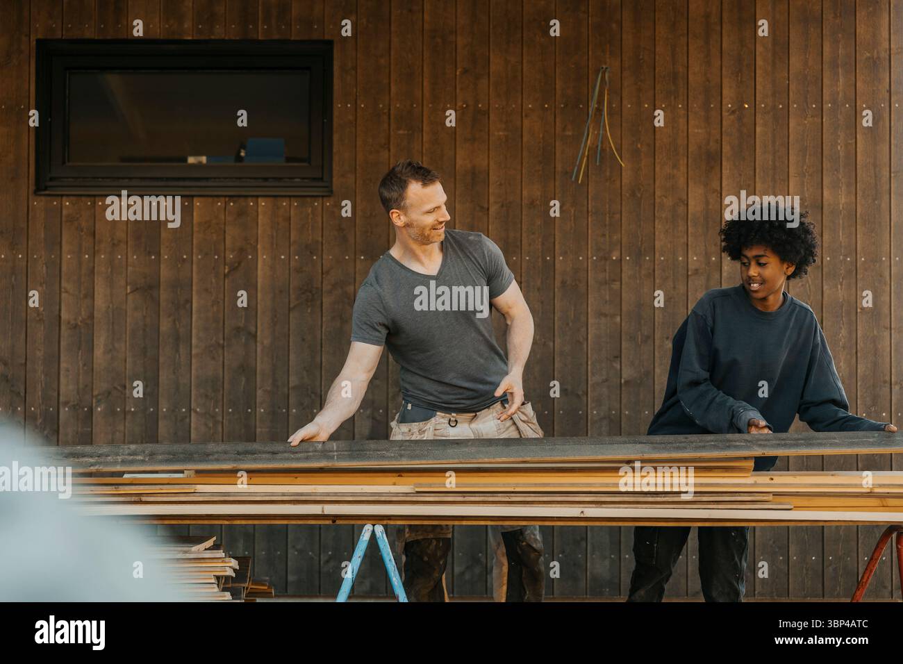 Der Sohn hilft dem Vater, während der Renovierung des Hauses Holzplanken auf dem Tisch zu halten Stockfoto