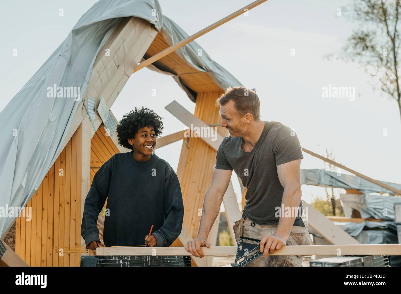 Lächelnder Junge, der mit Vater spricht, während er ein Haus im Hinterhof baut Stockfoto