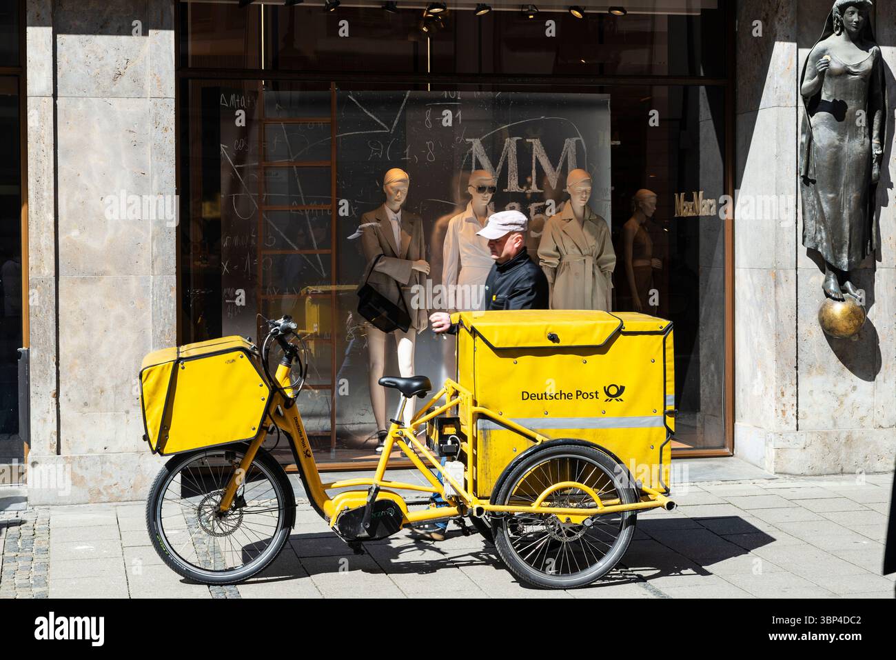 München - 5. April 2025: Postbote mit seinem Dreirad der Deutschen Post parkte auf einer Straße der Deutschen Post in München Stockfoto