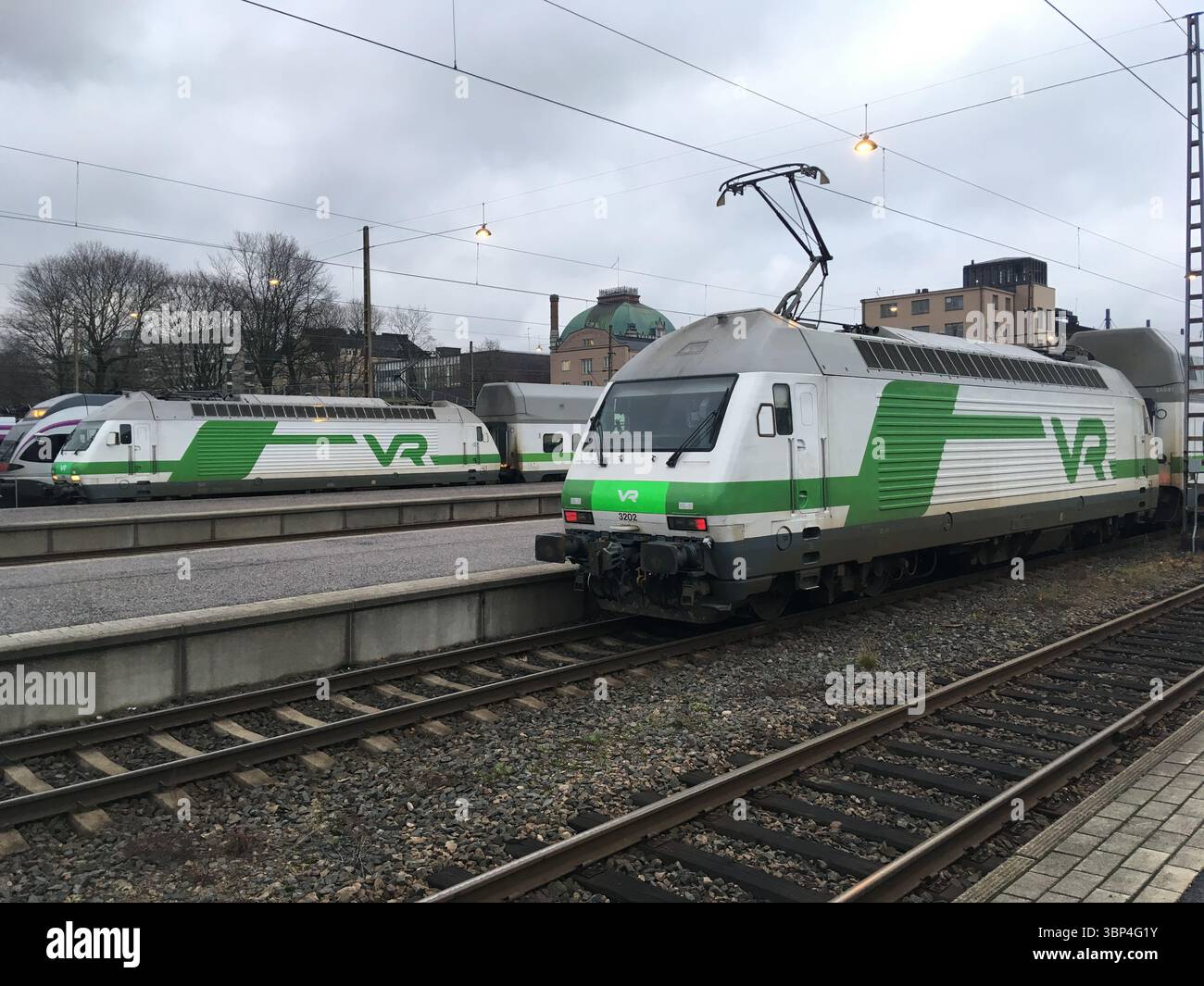 Außenaufnahmen von Zügen am Hauptbahnhof Helsinki, die historische Granitfassade, Laternenstatuen, Uhrenturm und städtische Bahnaktivitäten hervorheben. Stockfoto
