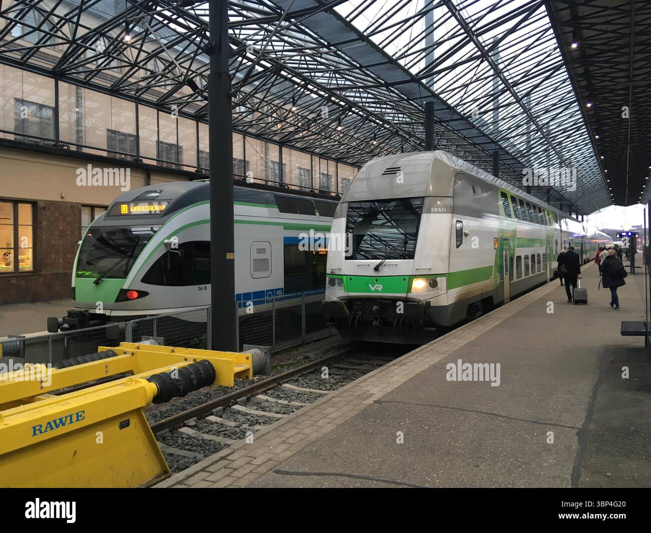 Außenaufnahmen von Zügen am Hauptbahnhof Helsinki, die historische Granitfassade, Laternenstatuen, Uhrenturm und städtische Bahnaktivitäten hervorheben. Stockfoto