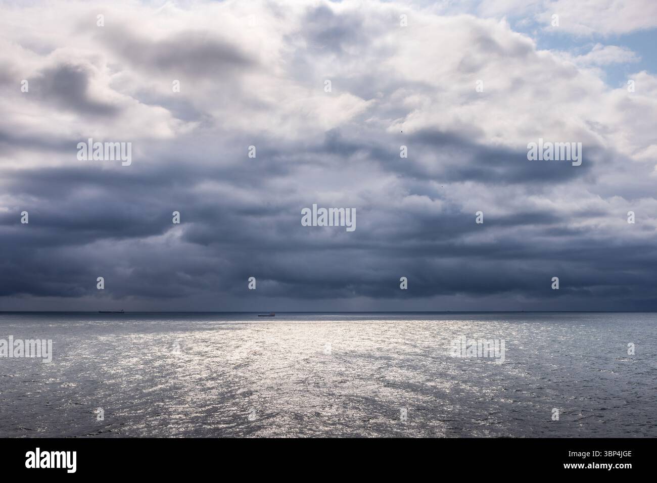 Stürmische Wolken sammeln sich über der Nordsee in der Nähe von Dänemark, von einem Kreuzfahrtschiff aus gesehen. Das silberne Wasser reflektiert Licht durch Brüche am dunklen Himmel. Stockfoto