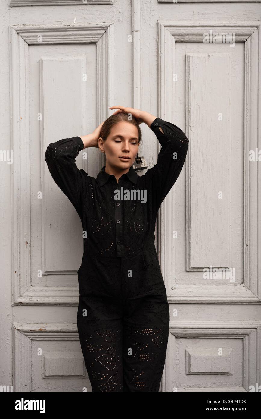 Fashion Woman Pose Door: Stilvolles Model steht mit Händen auf dem Kopf vor alten weißen Türen. Stockfoto