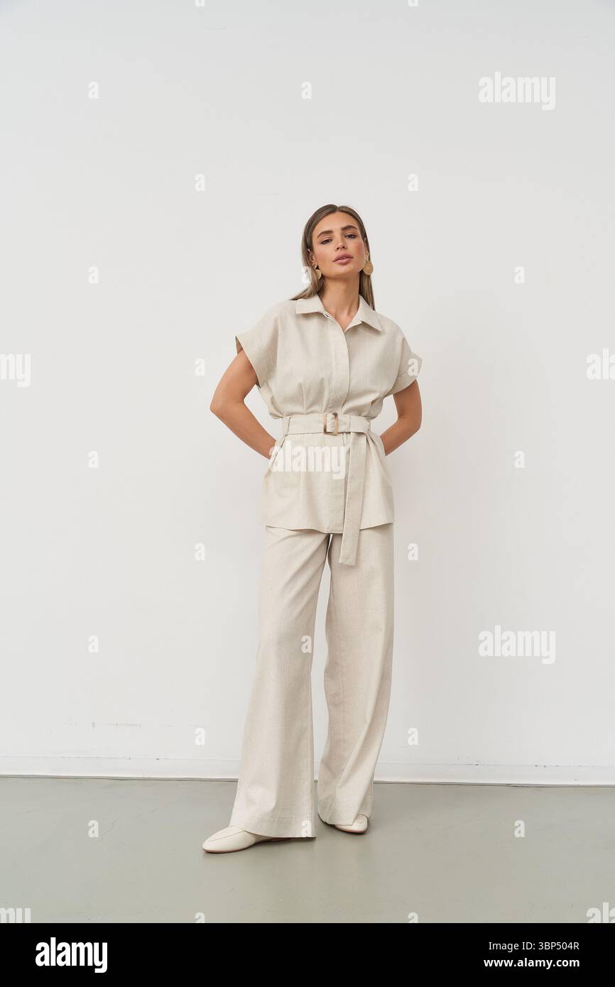 Eine selbstbewusste Frau steht in einem schicken Innenstudio und zeigt ihre modische Kleidung. Ihr stylisches Outfit besteht aus einem taillierten Oberteil und einer Hose mit weitem Bein, Stockfoto