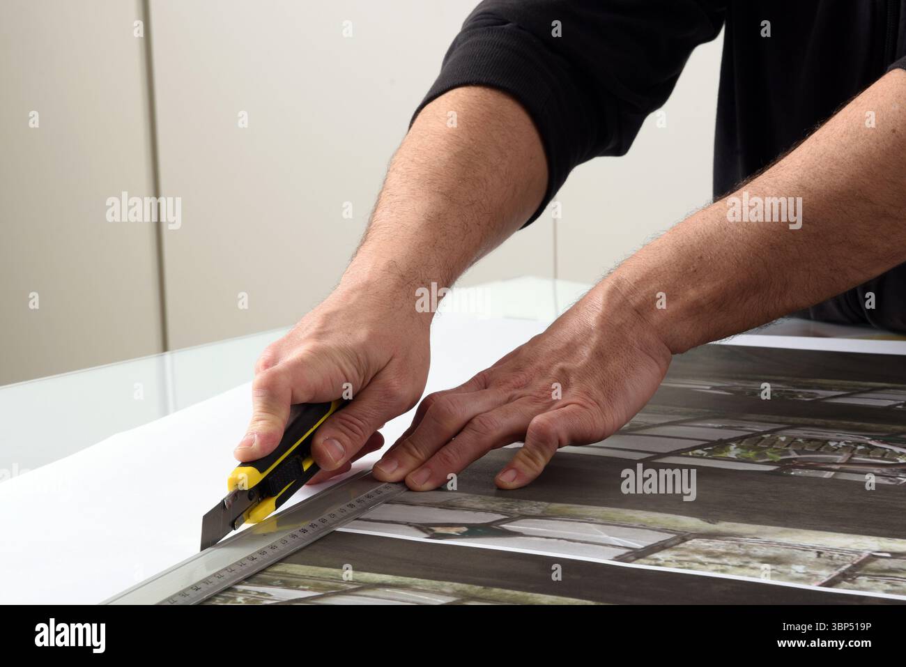 Nahaufnahme der Hände mit einem Cutter und einem Metalllineal zum Schneiden des Papierdrucks in einer Druckerei Stockfoto
