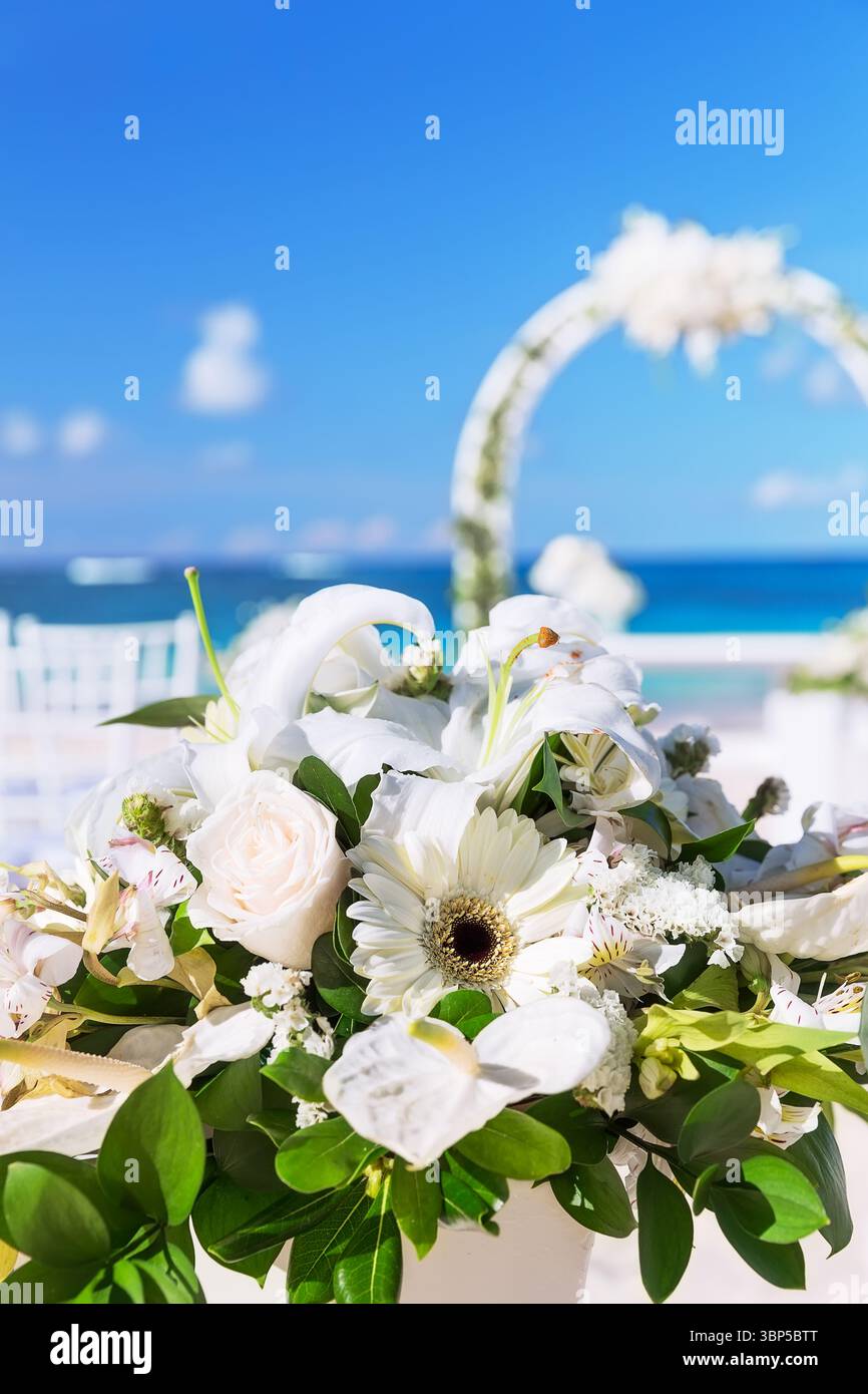 Blumenstrauß in einer Vase für die Hochzeitszeremonie und wunderschöner Hochzeitsbogen an einem tropischen Strand Stockfoto