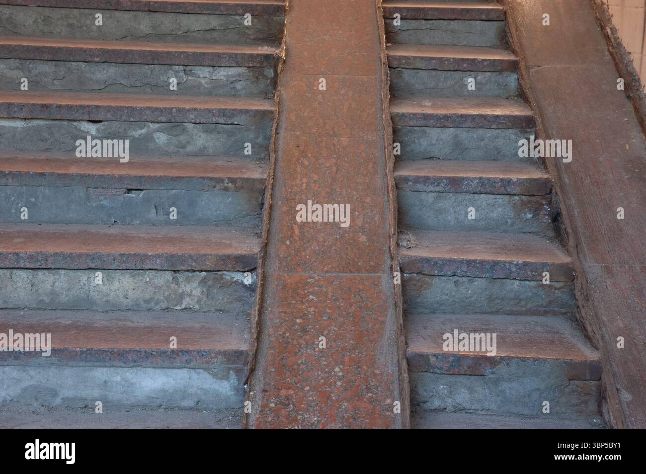 Alte Steintreppe mit Granitrampen für Kinderwagen, abgenutzt und verwittert. Zement zeigt Anzeichen von Alter und Zerfall, was auf eine langsame Verschlechterung im Laufe der Zeit hindeutet Stockfoto