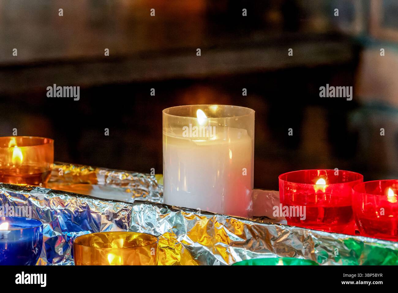 Farbenfrohe Votivkerzen, die in einer Kirche brennen, symbolisieren Gebet, Hoffnung und Hingabe in einer friedlichen religiösen Umgebung. Stockfoto
