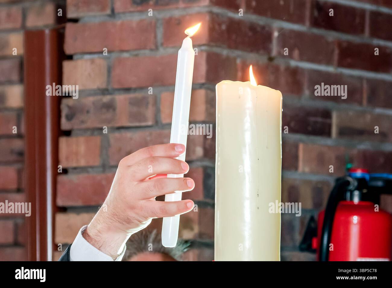 Eine Person, die während einer christlichen Taufzeremonie eine Kerze aus der Osterkerze zündet, die den Glauben und das spirituelle Licht symbolisiert. Stockfoto