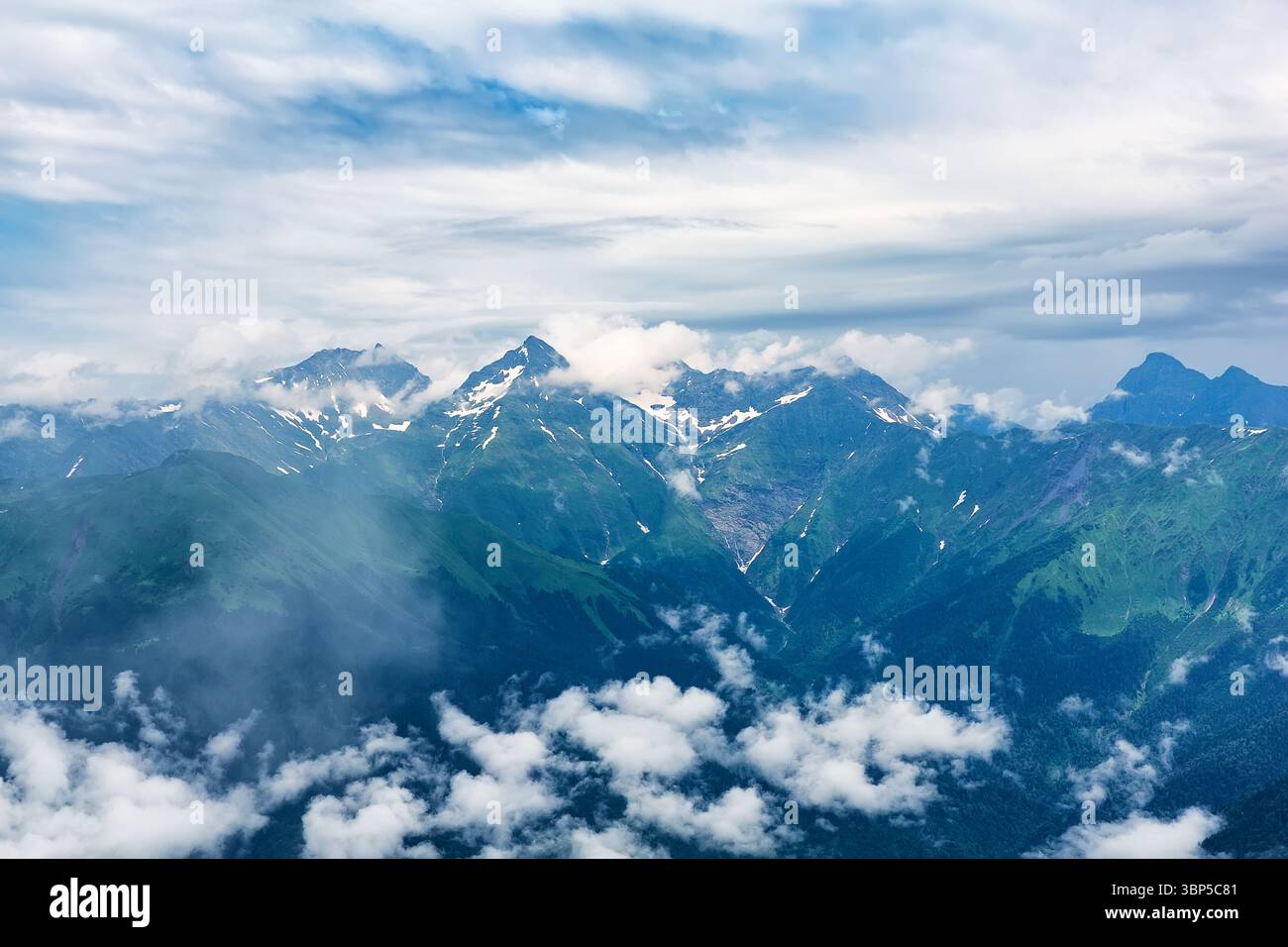 Neblige Berggipfel. Graue niedrige Wolken auf dem Gipfel des Berges. Gipfel von hohen Felsen mit Schnee in niedrigen Wolken. Stockfoto