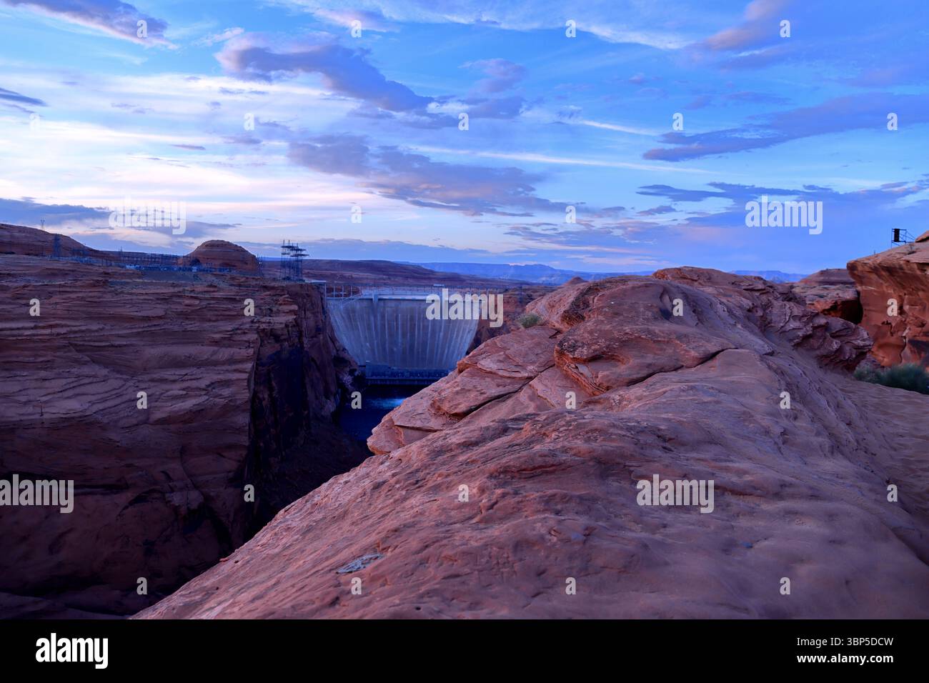 Der Glen Canyon Dam zieht eine kühne Linie zwischen zerklüftetem Sandstein und offenem Himmel, ein technisches Wunder, das in der wilden Stille der hohen Wüste in der Abenddämmerung eingebettet ist. Stockfoto