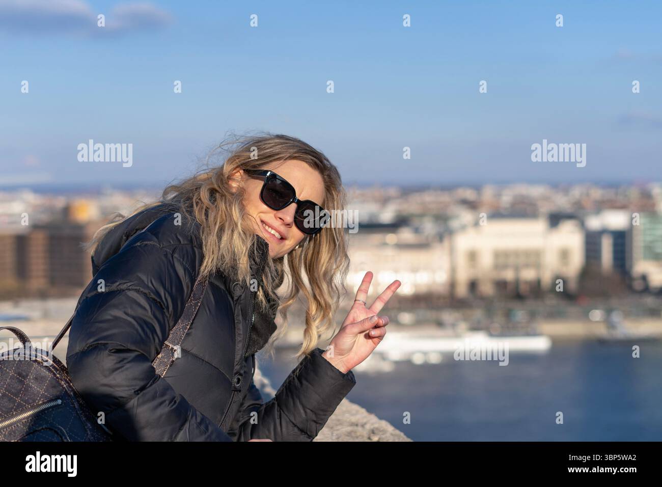 Touristische blonde Frau posiert mit Friedensschild über der Donau im Hintergrund des Winters Budapester Innenstadt Stockfoto