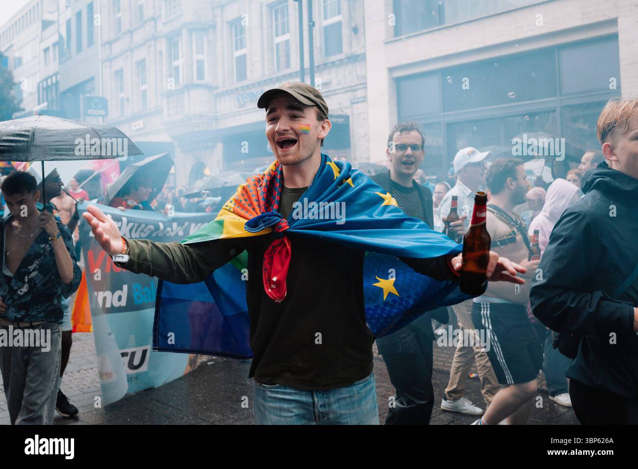 06.07.2025, CSD Köln 2025, Parade und Demonstration für Vielfalt und Gleichberechtigung Teilnehmer:in beim CSD Köln 2025 mit EU-Flagge als Umhang, Bierflasche und Regenschirm, begleitet von Demo-Gruppe mit Bannern. Köln Köln NRW Deutschland *** 06 07 2025, CSD Köln 2025, Parade und Demonstration für Vielfalt und Gleichberechtigung Teilnehmer auf CSD Köln 2025 mit EU-Flagge als cape, Bierflasche und Regenschirm, begleitet von Demo-Gruppe mit Bannern Köln Köln NRW Deutschland Stockfoto