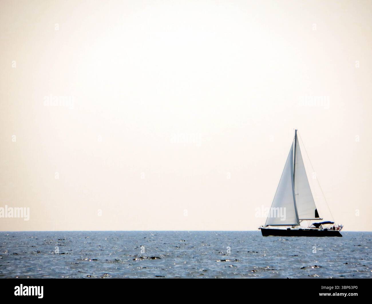 Eine Segelyacht bewegt sich anmutig über das ruhige Meer, ihre weißen Segel fangen die Brise unter klarem Himmel. Stockfoto