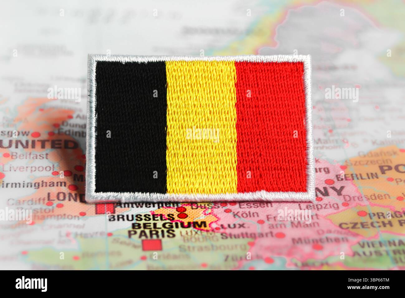 Aufgestickte belgische Flagge auf Stoff, über Brüssel auf einer Weltkarte. Symbol des belgischen Stolzes und der Reisekultur. Stockfoto