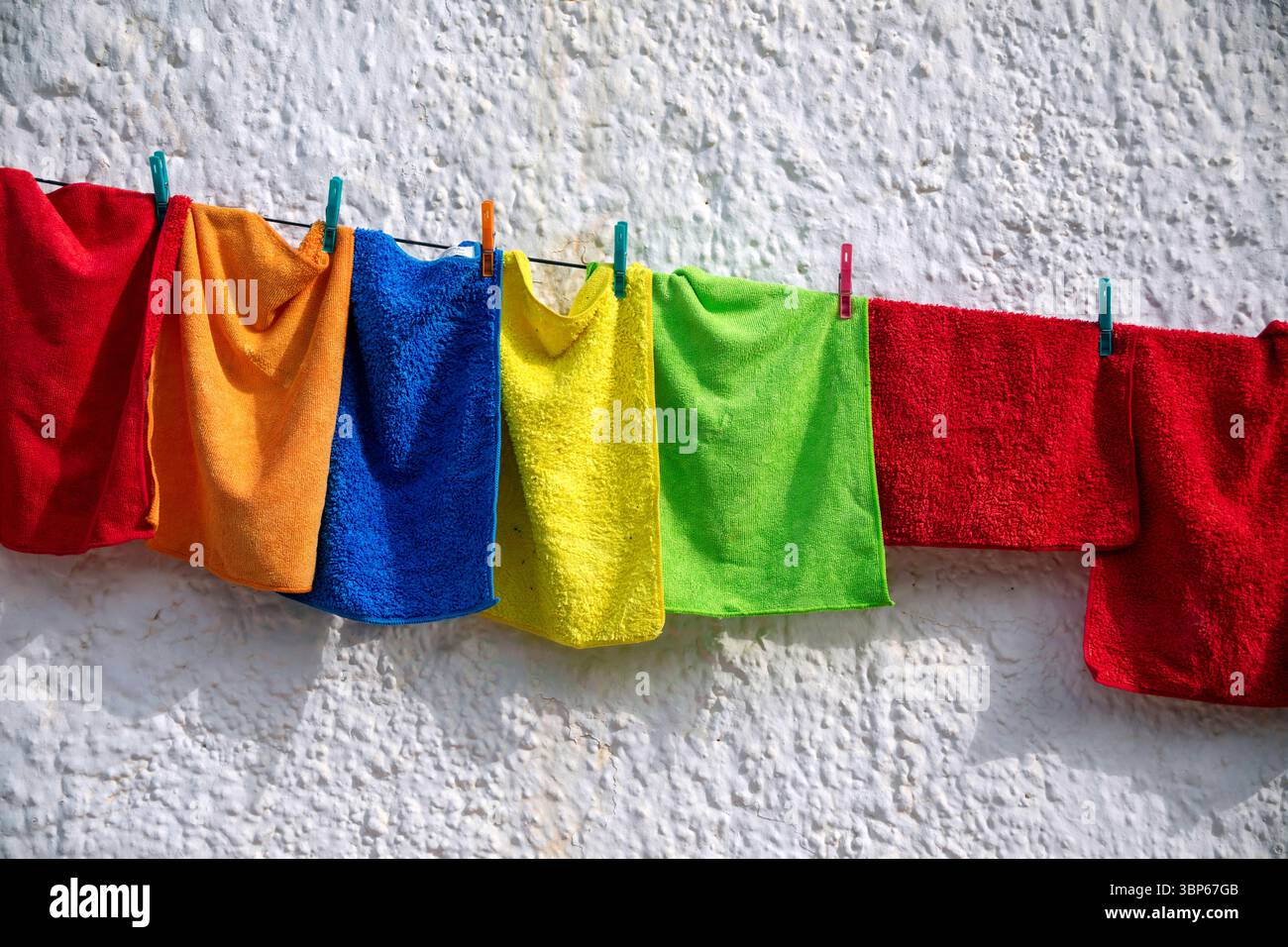 Reinigungstücher in verschiedenen gesättigten Farben hängen an einem Seil mit Wäschespins an einer weißen Wand Stockfoto