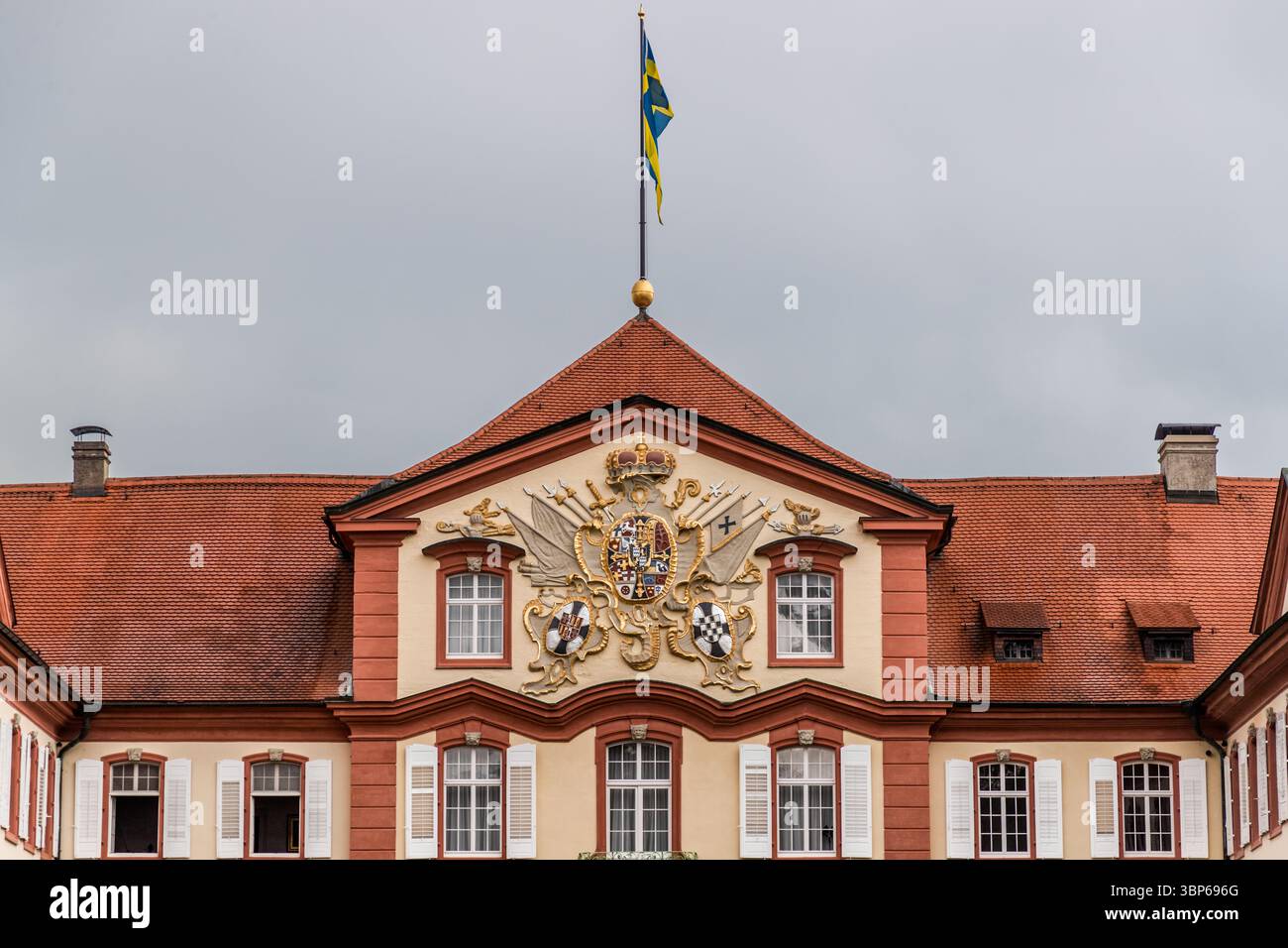 Nahaufnahme der zentralen Fassade des barocken Schlosses Mainau auf der Insel Mainau bei Konstanz, Baden-Württemberg. Die schwedische Flagge fliegt über dem prächtigen Wappen, was die Verbindung der Insel zur Familie Bernadotte signalisiert Stockfoto
