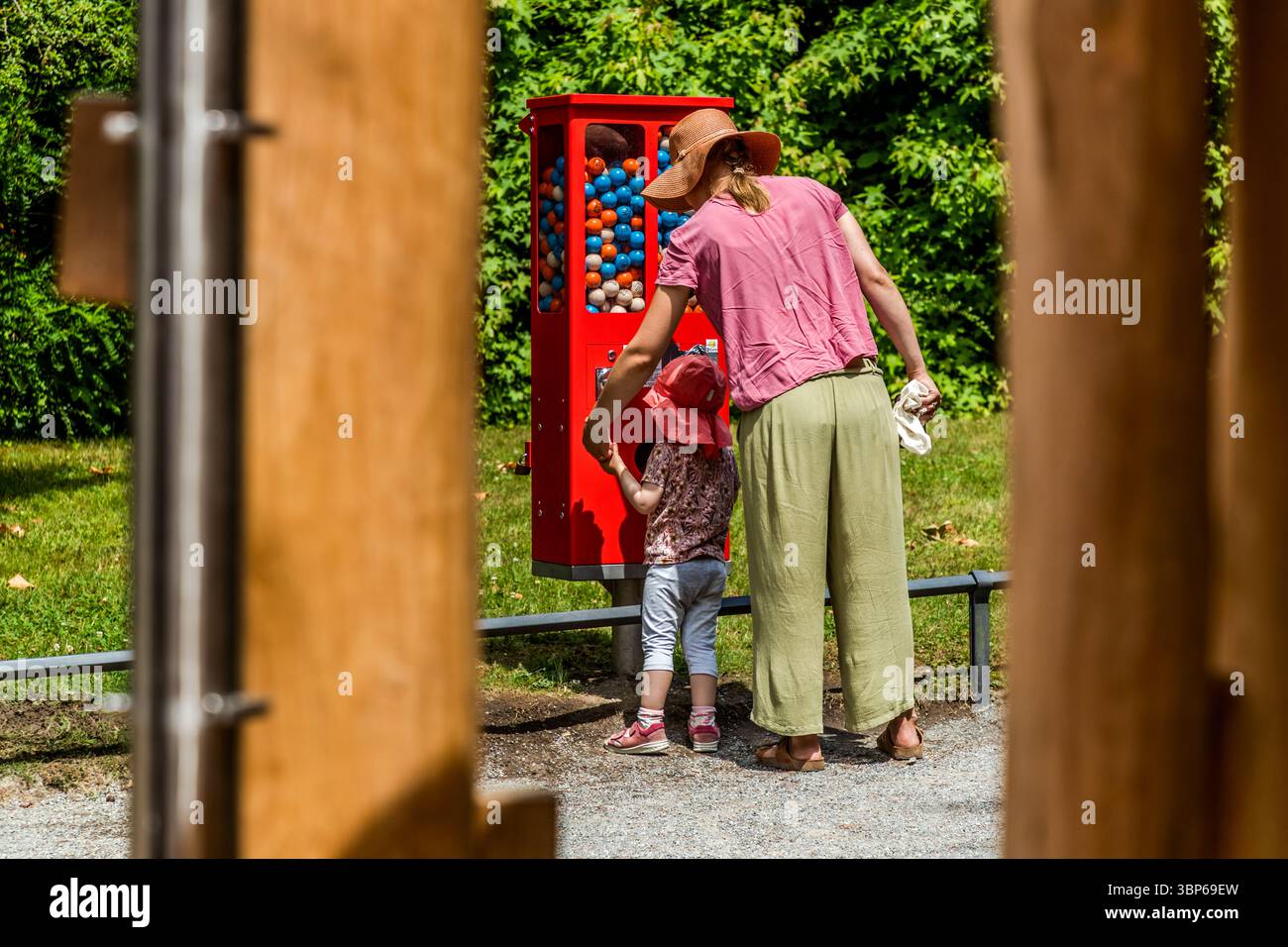 Eine Frau und ein kleines Kind stehen vor einer roten Maschine mit bunten Kugeln auf der Ballbahn auf der Insel Mainau. Das Kind versucht, einen Ball aus der Maschine zu bekommen, unterstützt von der Frau. Baden-Württemberg, Deutschland Stockfoto