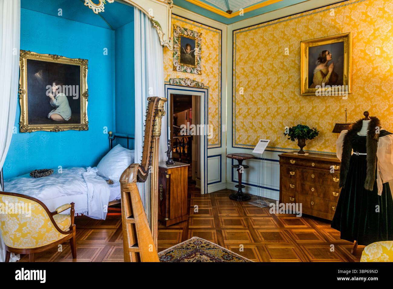 Ein Blick in einen prächtigen historischen Raum auf Schloss Arenenberg in Salenstein, Thurgau, Schweiz. Dieses detailreiche Interieur, das einst von Königin Hortense de Beauharnais bewohnt wurde, verfügt über Originalmöbel, Kunstwerke wie die Gemälde an den Wänden, eine Harfe und historische Kleidung auf einer Schaufensterpuppe. Es vermittelt einen anschaulichen Eindruck von Leben und Stil der ehemaligen Bewohner und ist heute Teil des Arenenberg-Museums Stockfoto