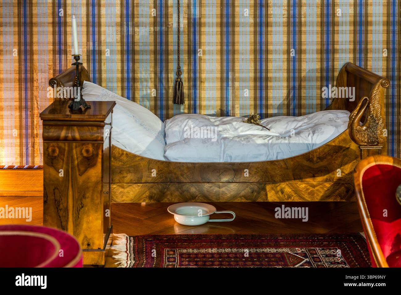 Ein historisches Schlafzimmer im Schloss Arenenberg in Salenstein, Thurgau, Schweiz, verfügt über ein Bett mit kunstvollen Schnitzereien, einen Nachttisch mit Kerzenleuchter und einen Kammertopf auf dem Holzboden. Der Raum, der einst von Hortense de Beauharnais und ihrem Sohn Napoleon III. Bewohnt wurde, bietet einen Einblick in die Wohnkultur des 19. Jahrhunderts Stockfoto