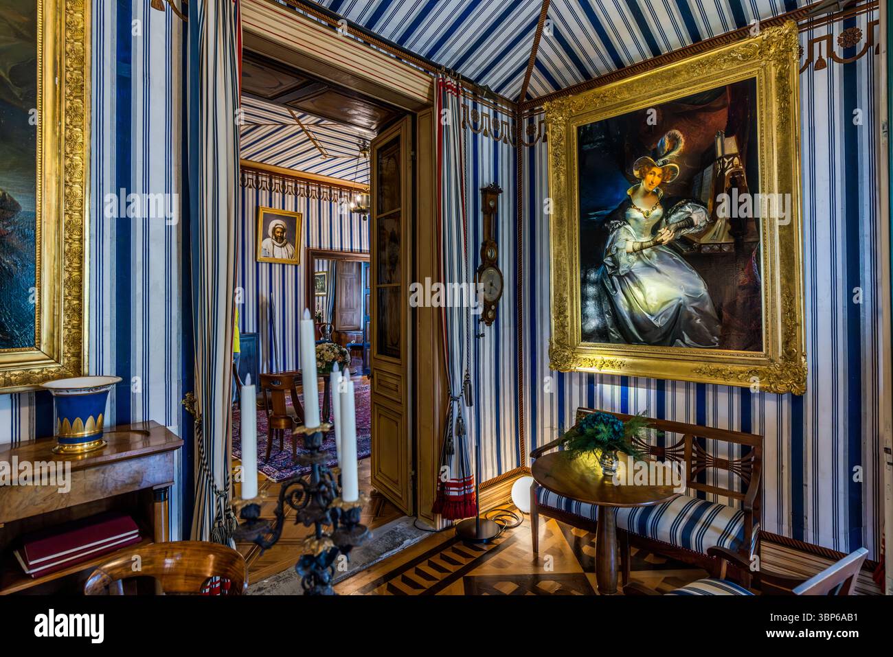 Zeltstube auf Schloss Arenenberg in Salenstein, Thurgau, Schweiz. Das Zimmer ist im Empire-Stil eingerichtet, mit charakteristischen blau-weiß gestreiften Wänden und Decken, die an ein Zelt erinnern. An den Wänden hängen große Porträts, darunter eines von Napoleon Bonaparte und Hortense de Beauharnais. Möbel wie ein Klavier, ein Kerzenleuchter und passende Stühle runden das historische Ambiente ab. Dieser Raum zeugt von der Zeit, als Hortense de Beauharnais, Königin von Holland und Napoleons Stieftochter, hier lebte. Arenenberg, Salenstein, Thurgau, Schweiz Stockfoto