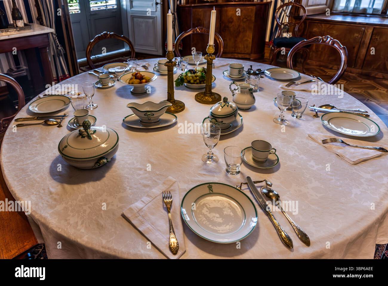 Ein elegant gedeckter Esstisch im Schloss Arenenberg in Salenstein, Thurgau, Schweiz. Das Porzellan von Limoge ist mit einem gekrönten N-Monogramm verziert, das auf die Familie Bonaparte verweist, die hier wohnte. Goldfarbenes Besteck, feine Gläser und eine Obstschale runden das historische Ambiente eines festlichen Tisches ab Stockfoto