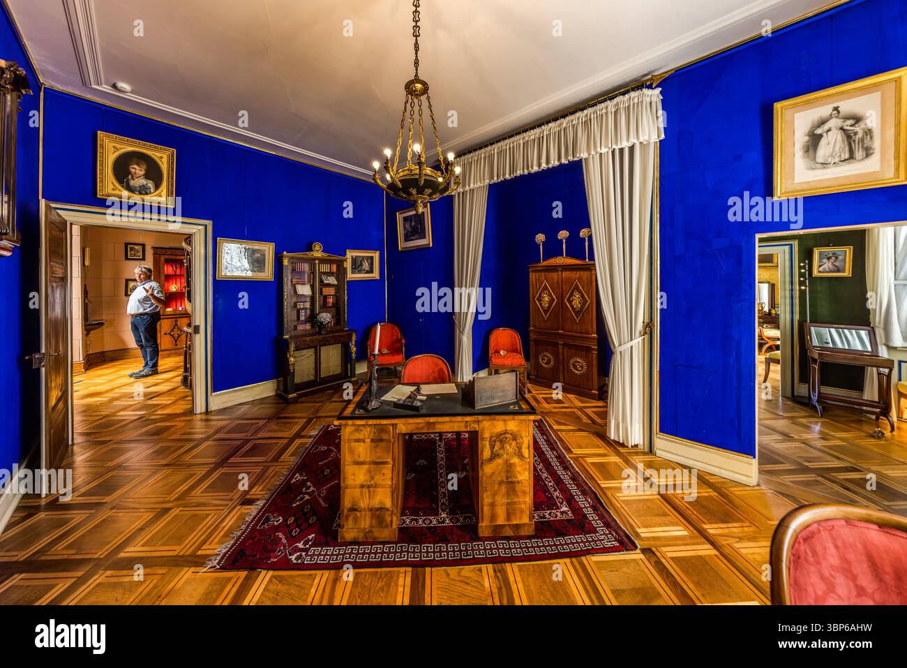 Eine historische Studie mit blauen Wänden und einem großen Schreibtisch im Napoleon Museum. Museumsdirektor Dominik Gügel steht in einer Tür und schaut in den Raum. Das Zimmer befindet sich im Schloss Arenenberg in Salenstein, Thurgau, Schweiz. Stockfoto