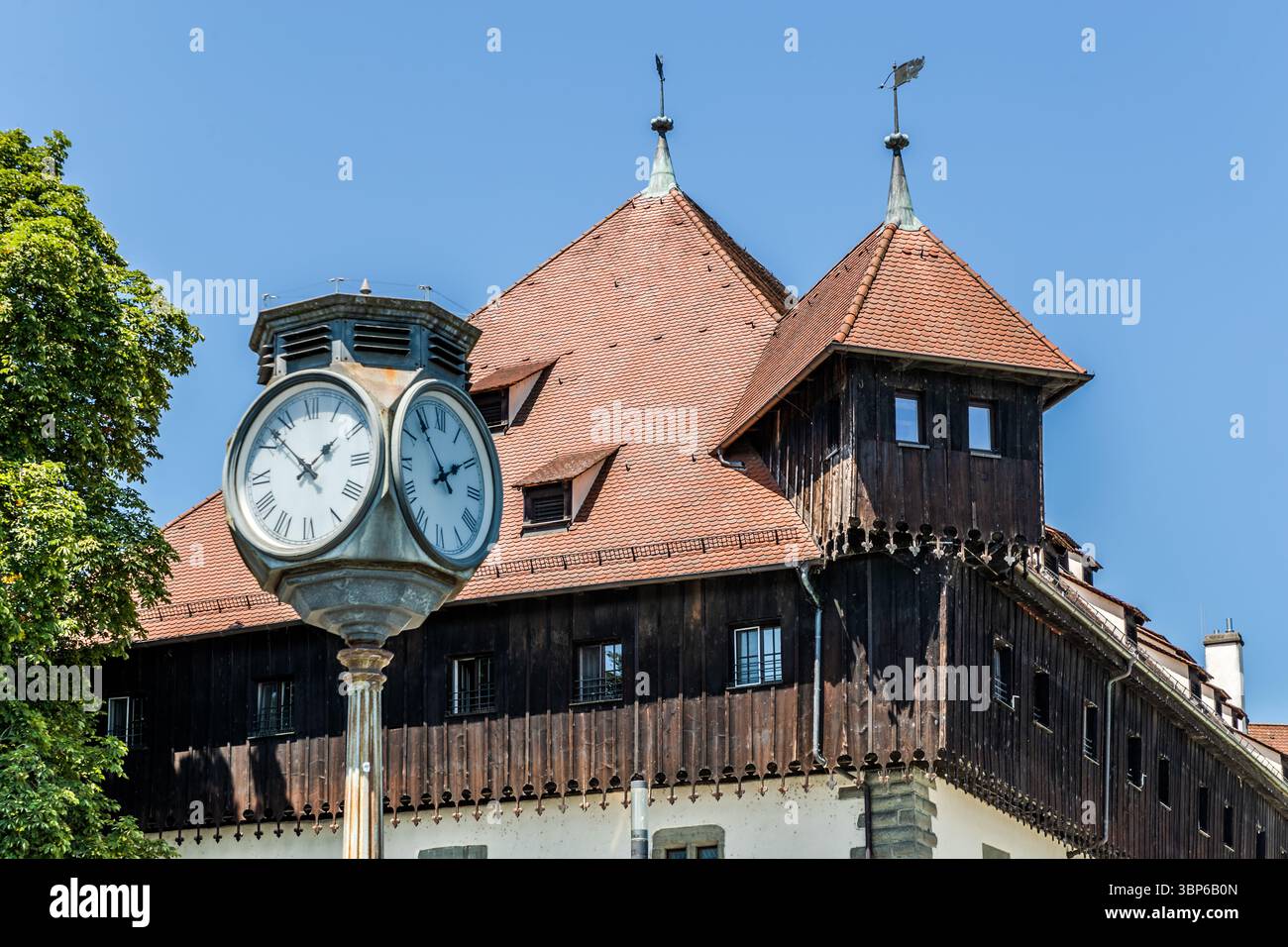 Das Gemeindegebäude in Konstanz mit einem gekachelten Dach, Holzwänden und zwei Türmen mit Wetterfahnen. Im Vordergrund steht eine große Uhr mit römischen Zahlen. Hafenstraße, Konstanz, Baden-Württemberg, Deutschland Stockfoto