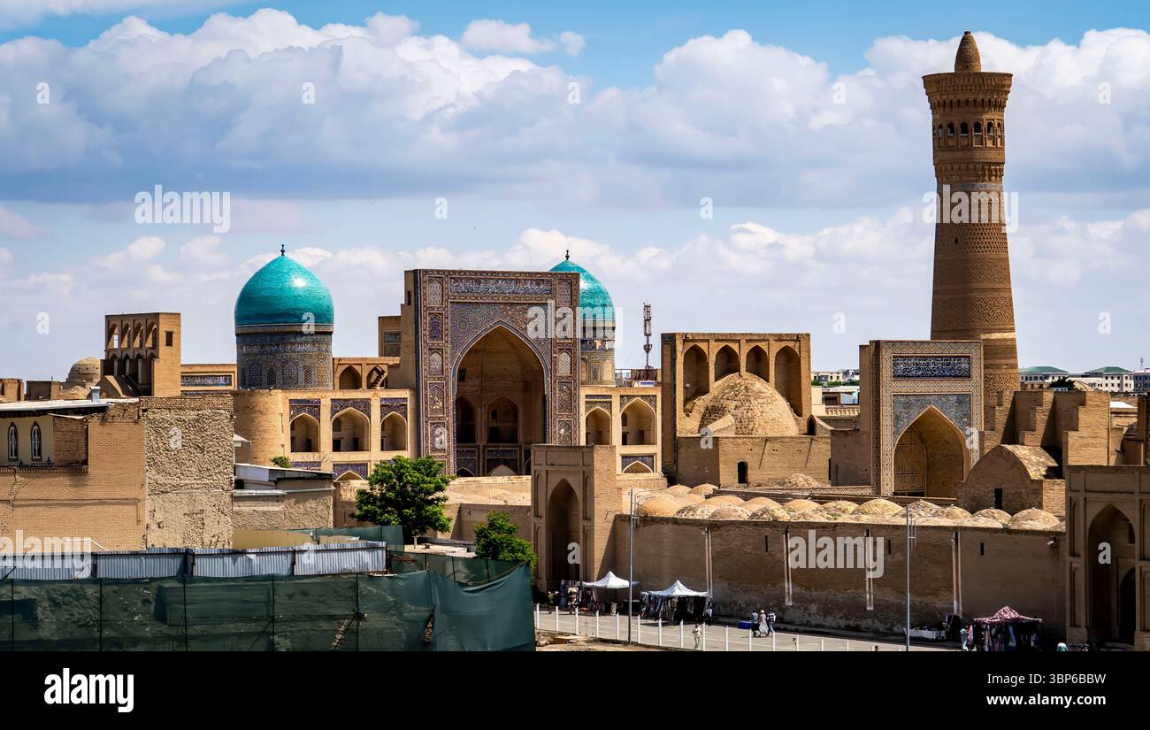 Ein Panoramablick auf die historische Architektur in Buchara, Usbekistan, mit Kuppelbauten mit türkisfarbenen Dächern und einem hohen Minarett vor einer blauen Ske Stockfoto