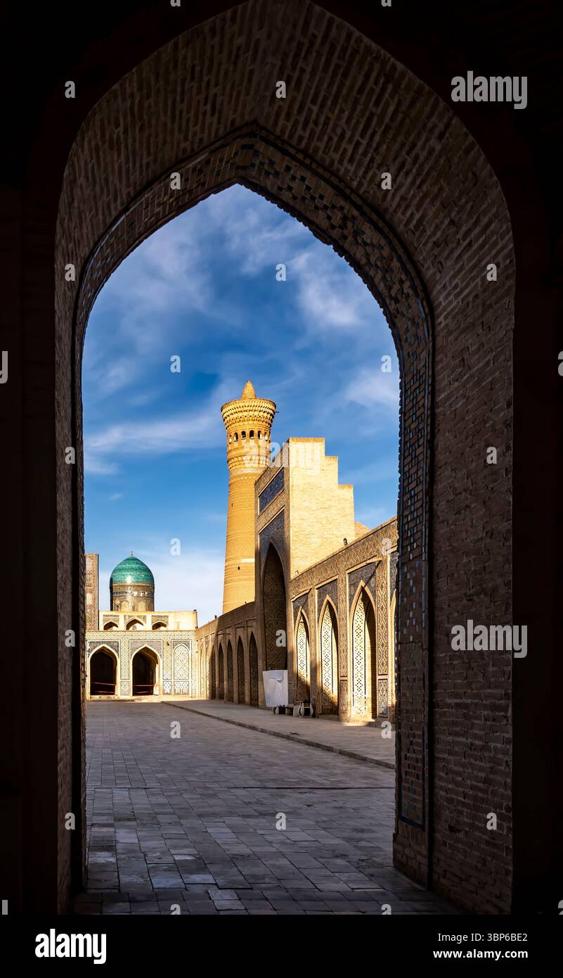 Ein atemberaubender Blick durch einen Bogengang, der einen historischen Komplex mit einem hohen Minarett und Kuppelbauten unter einem blauen Himmel zeigt. Das komplizierte Mauerwerk Stockfoto