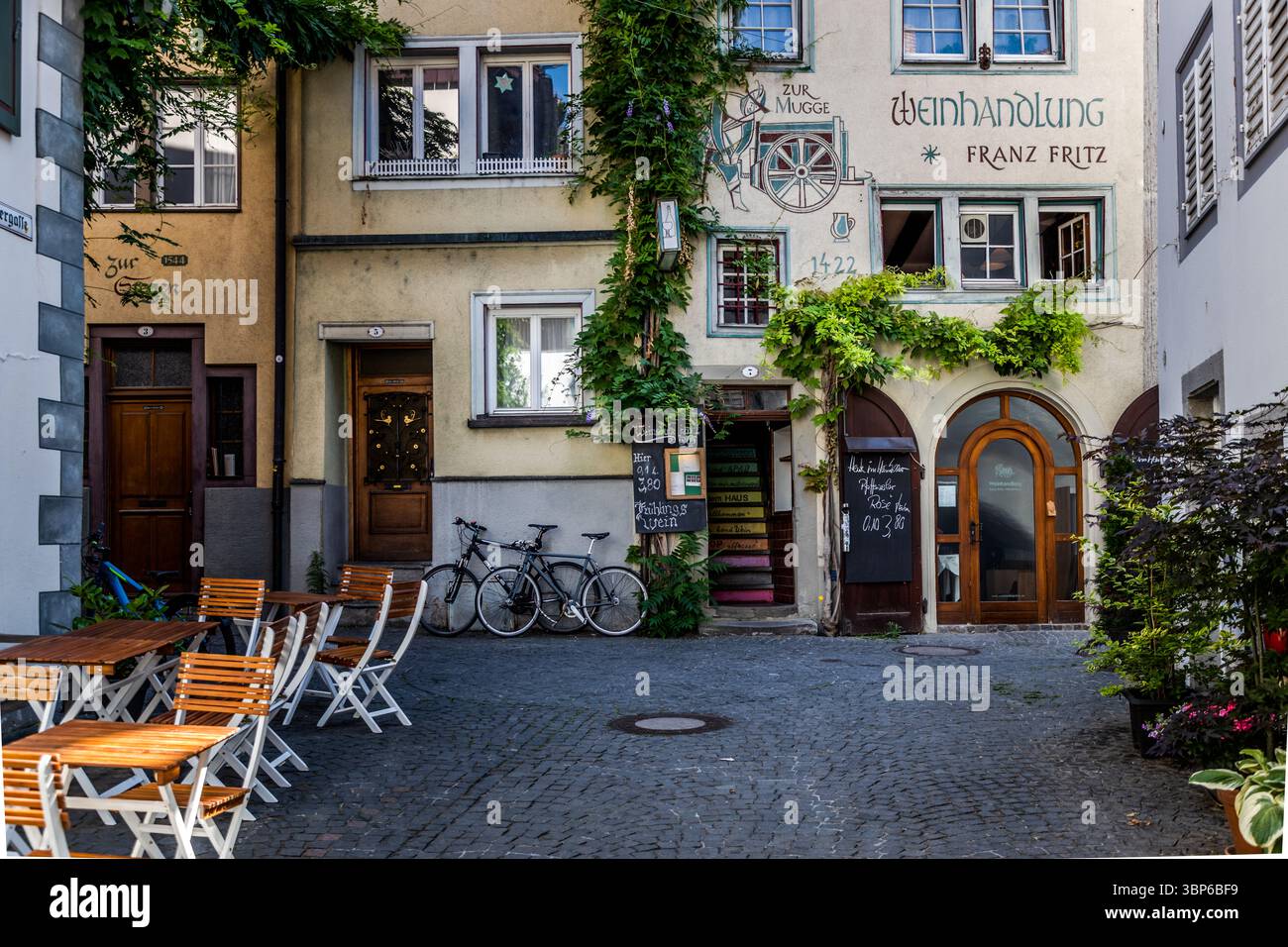 Historische Gebäude prägen die Schreibergasse in Konstanz. Tische und Stühle für das Catering im Freien stehen auf dem Kopfsteinpflaster. Zwei Fahrräder lehnen sich an eine Hauswand. Schreibergasse, Konstanz, Baden-Württemberg, Deutschland Stockfoto
