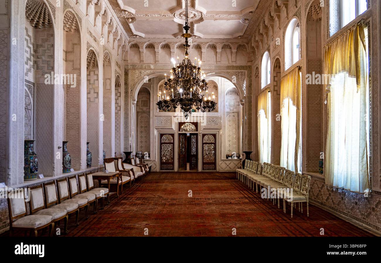 Das elegante Interieur eines großen Saals mit kunstvoller Architektur, hohen Fenstern mit fließenden Vorhängen und einem großen Kronleuchter. Das Zimmer ist mit einem schmückenden Dekor versehen Stockfoto