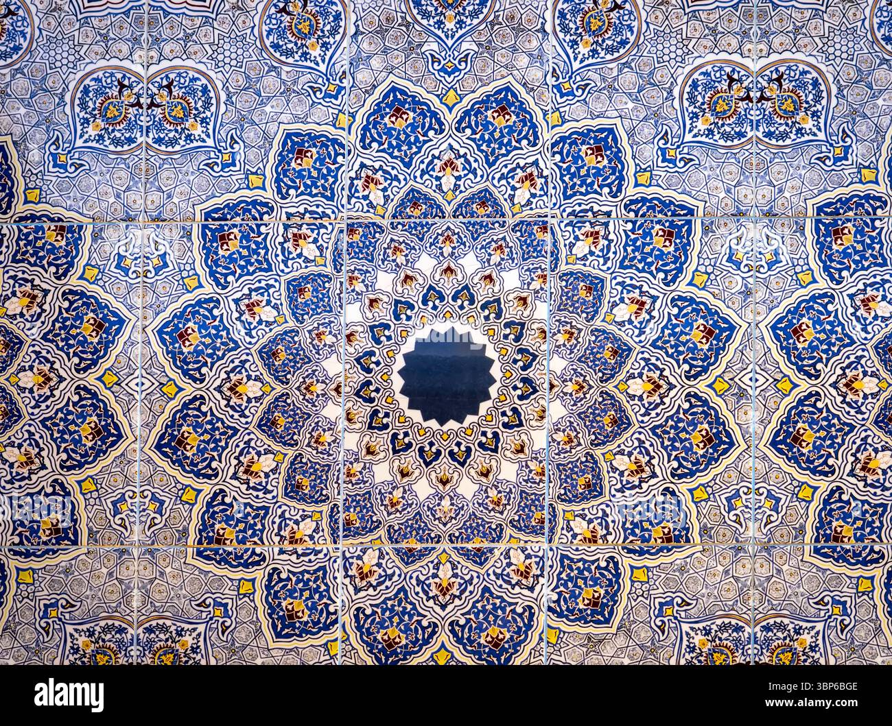 Ein lebendiges und kompliziertes Mosaik mit geometrischen Mustern in Blau, Gelb und weiß. Die Konstruktion wird von einem zentralen Punkt aus abgestrahlt und erzeugt ein mesm Stockfoto