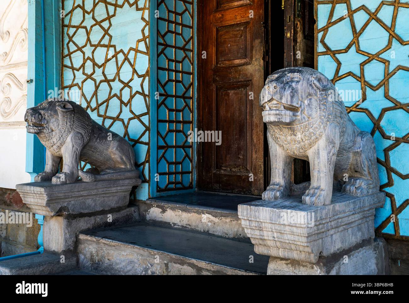Zwei aufwändig geschnitzte Löwenstatuen aus Stein bewachen den Eingang eines Gebäudes mit einer blauen Wand und einer Holztür, die das traditionelle architektonische El darstellt Stockfoto